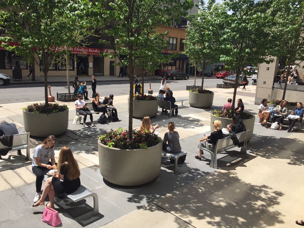 Planted containers and mature trees in the occupied Fashion Institute of Technology plaza